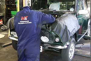 distance view of a mechanic working under the bonnet of a classic british racing green mini 1275 gt getting a service