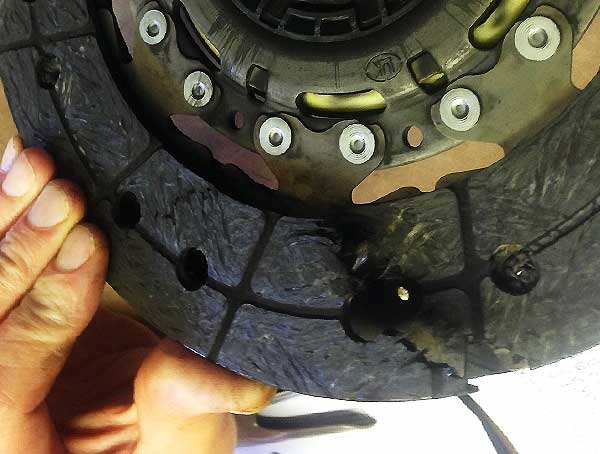close up angled side view of a broken clutch plate that has completly split down one side highlighted by our clutch specialit pulling open the crack with his blue gloves