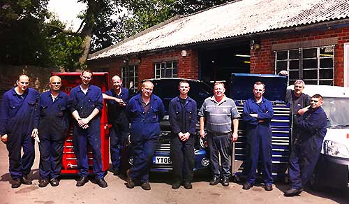 distance view of our sheffield garage and team all lined up wearing blue overalls and the company logo smiling happily outside the garage entrance