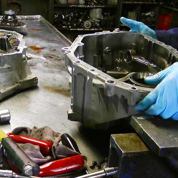 distance view of a dismantled ford gearbox showing the bell housing held and examined by an expert and various components on his bench
