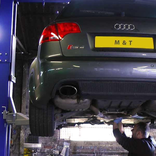 distance rear slight under and over view of a gunmetal grey coloured audi rs4 car on a ramp high in the air part way through servicing by a m and t mechanic